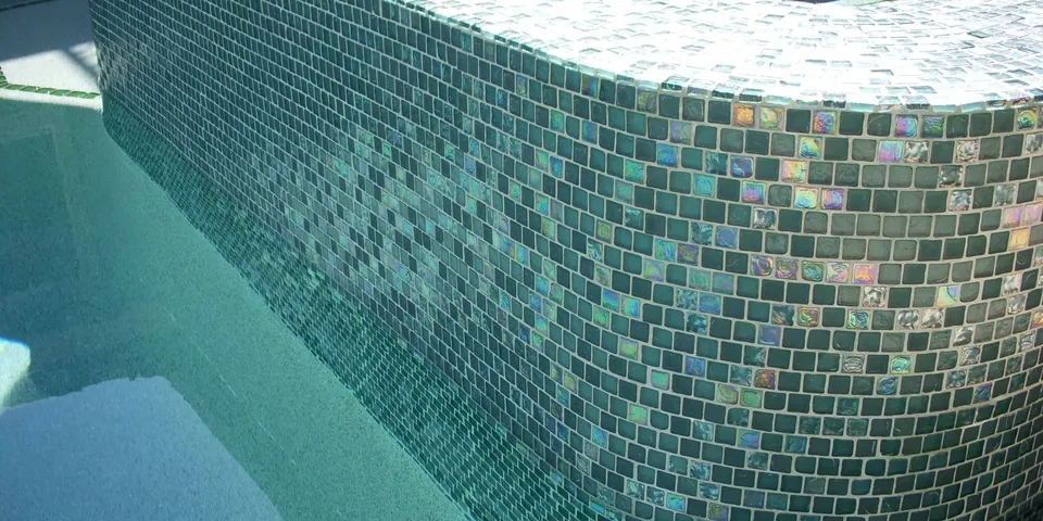 Spa wall clad in iridescent glass tile above the pool