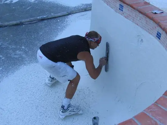 Plasterer troweling a new white finish on a pool wall
