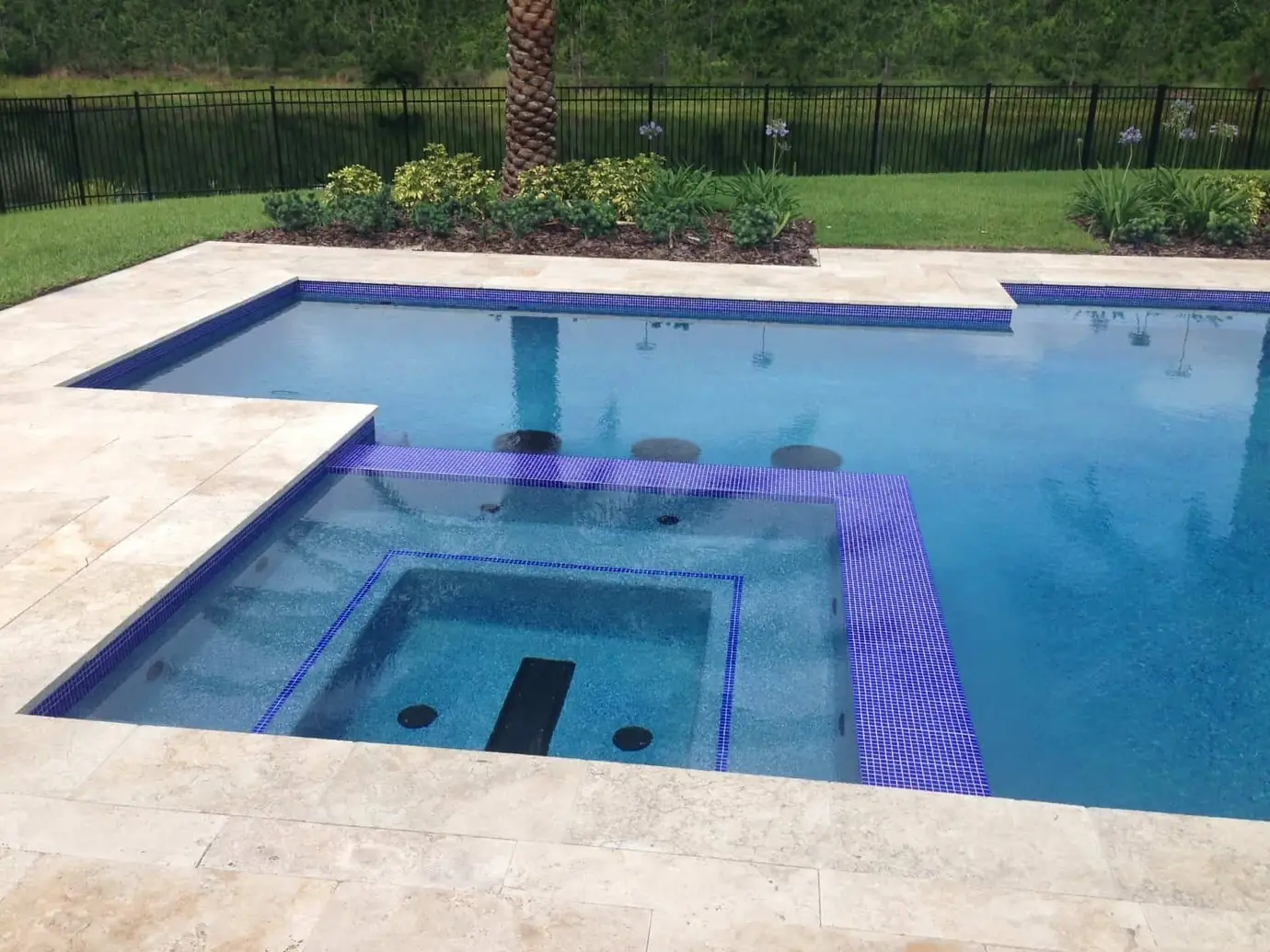 Rectangular pool and raised spa with purple waterline tile and travertine deck