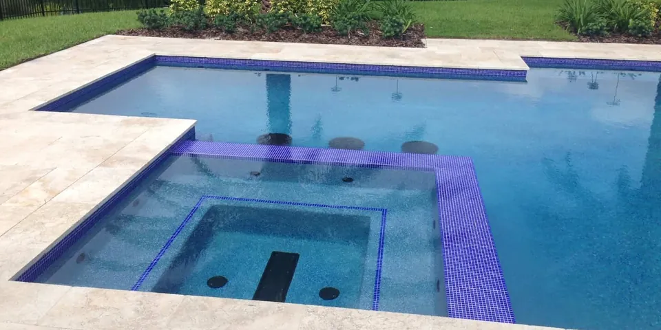 Rectangular pool and raised spa with purple waterline tile and travertine deck