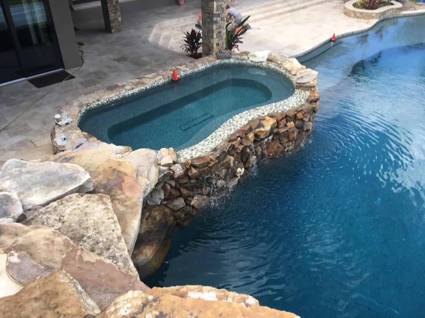 Raised stone spa spilling into a dark blue freeform pool