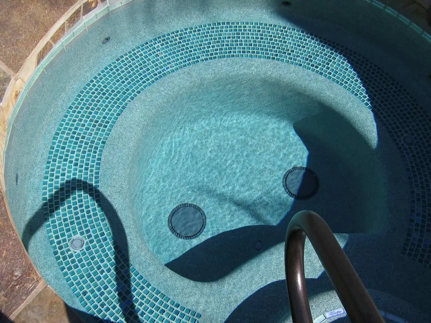 Round spa with green glass mosaic tile and a handrail