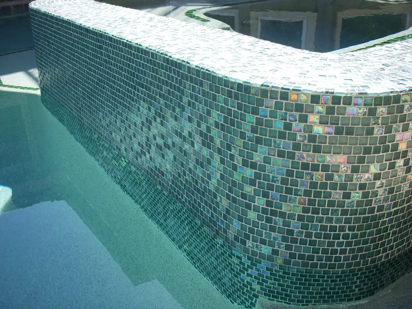 Spa wall clad in iridescent glass tile above the pool