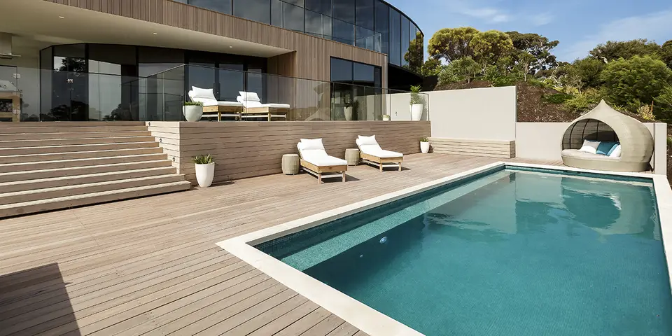 Modern swimming pool with wooden deck, lounge chairs, and a stylish outdoor seating area, reflecting Classic Marcite's pool resurfacing services in Jacksonville Beach.