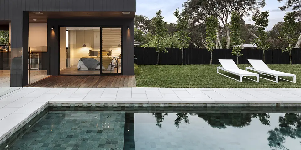 Modern swimming pool with clear water, white lounge chairs, and a contemporary home in the background, highlighting pool resurfacing services by Classic Marcite in Jacksonville Beach.