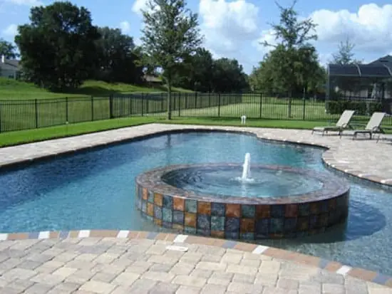 Freeform pool with a mosaic tile fountain and paver deck