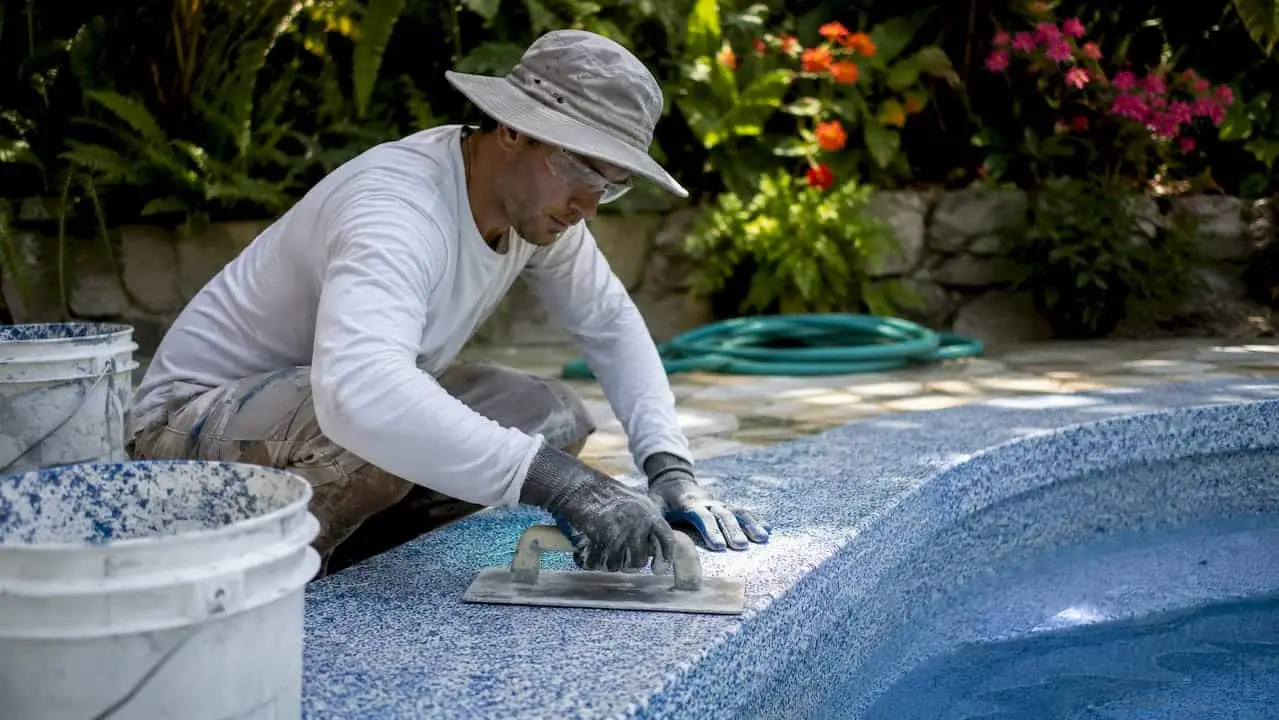 Contractor applying quartz pool finish in backyard