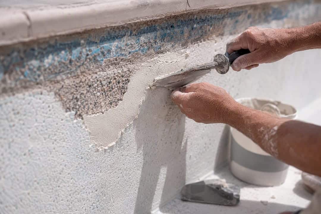 Hands patching pool plaster with undercut edge